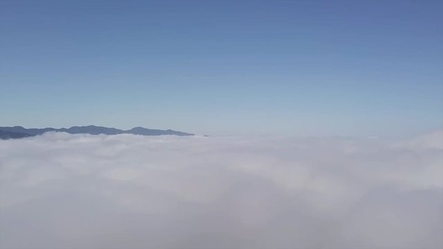 Aerial cloudline, calm fluffy clouds drift along on calm day on mountaintops.