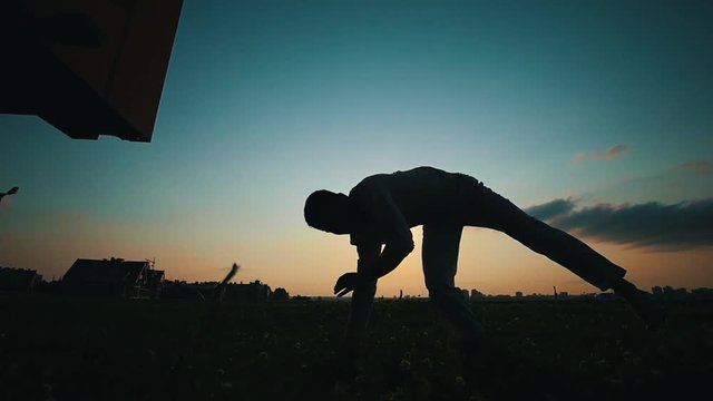 Silhouette of a sporty man who shows cool tricks of capoeira dance on the background, summer sunset