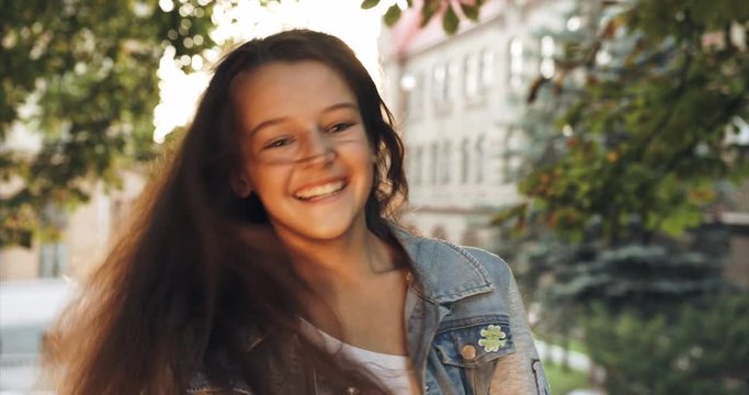 Funny little brunette girl is shaking her head and playing with long hair. Portrait of the smiling child. 4k footage.