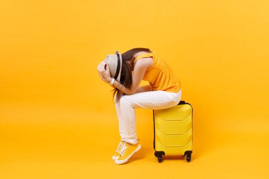 Upset tourist woman in summer casual clothes sit on suitcase put hands on head isolated on yellow orange background. Female traveling abroad to travel on weekends getaway. Air flight journey concept.