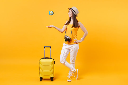 Traveler tourist woman in summer hat with suitcase throw up globe isolated on yellow orange background. Female passenger traveling abroad to travel on weekends getaway. Air flight journey concept.