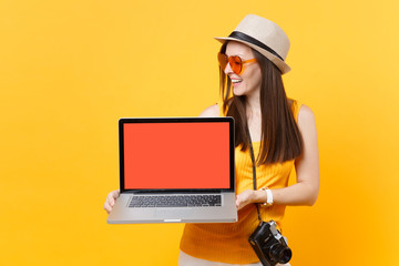 Traveler tourist woman holding laptop pc computer with blank black empty screen isolated on yellow orange background. Female traveling abroad to travel on weekends getaway. Air flight journey concept.