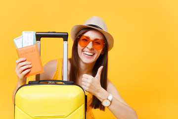 Traveler tourist woman in summer casual clothes, hat with suitcase showing thumb up isolated on yellow background. Passenger traveling abroad to travel on weekends getaway. Air flight journey concept.
