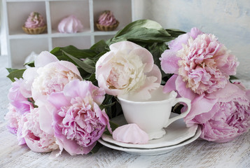 on the table a bouquet of pink peonies, a mug and pink meringue pies
