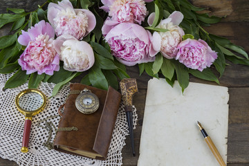 on a table of dark wood a bouquet of pink peonies, a smoking pipe, a magnifying glass, a magnifying glass, a book, a pocket watch, a sheet of old paper and a fountain pen