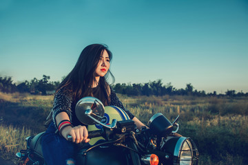 Fototapeta na wymiar Young woman drive with motorcycle on street, enjoying freedom and active lifestyle, having fun on a bikers tour on sunset background.