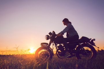 Plakat Young woman drive with motorcycle on street, enjoying freedom and active lifestyle, having fun on a bikers tour on sunset background.