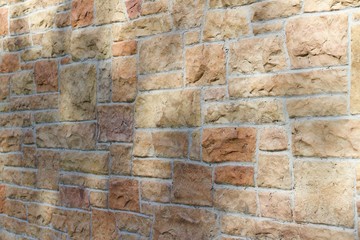 Aged fossiliferous limestone brick wall background in shades of orange, pink, yellow, and beige showing late day tree shadows (angle view)