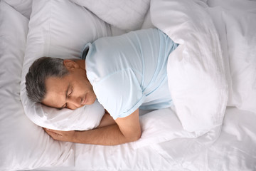 Man sleeping on comfortable pillow in bed at home, top view