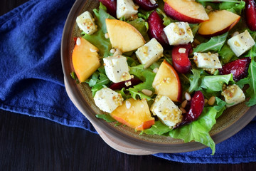 Fruit salad with arugula, plums, nectarines and soft cheese on a plate