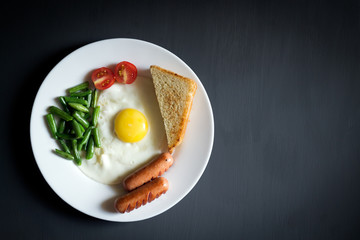 A hearty breakfast on a white plate on a black background. Scrambled eggs, bread, sausages, beans, cherry tomato.