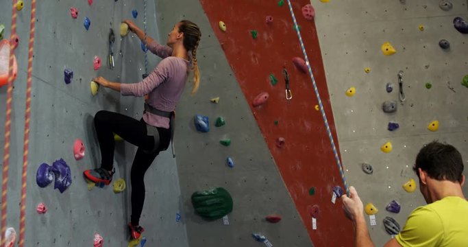 Coach assisting a woman in climbing the artificial wall 4k