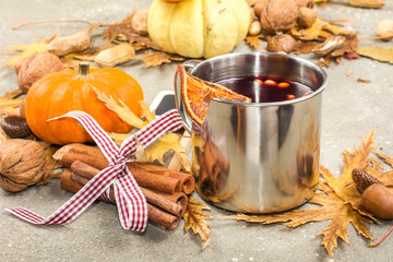 Mulled wine in metal rustic mug with spices and citrus fruits decorated with autumn leaves and pumpkin