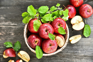 A lot of fresh Royal Red Gala apples with green leaf and water drop in basket on wooden background.