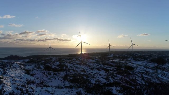 Aerial footage of large wind turbines roating with the sun set in the background