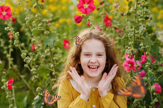 Laughing curly girl with a butterfly on her hair showing white teeth.
