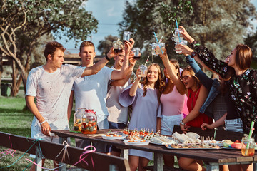 Group of happy friends having fun together celebrating a birthday at the outdoor park. Joyful friends cheering with juice at picnic party outdoor.