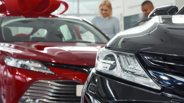 Happy young couple looking inside a new automobile for sale at the dealership. Cheerful woman and her man examining cars before buying. Consumerism, automotive retail concept.