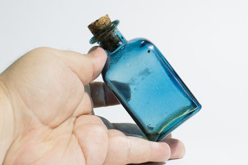 frasco botella de cristal color azul con tapón de corcho sobre una mano y fondo blanco	