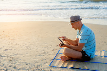 Senior man working on his laptop on the beach sea during sunset, freelancer concept in travel