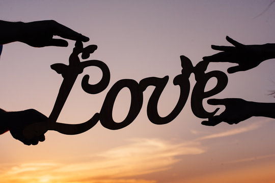bride and groom holding  the word love.
the couple holds in  hands a wooden love inscription.
