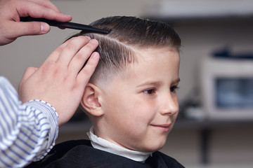 Barber making a haircut to a boy using hairbrush.