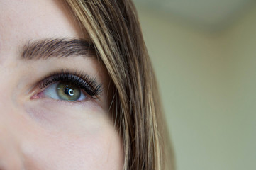 Eyelash extension procedure. Young beautiful woman eye with long false eyelashes. Close up macro...