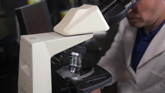 Lab technician examines sample through microscope.