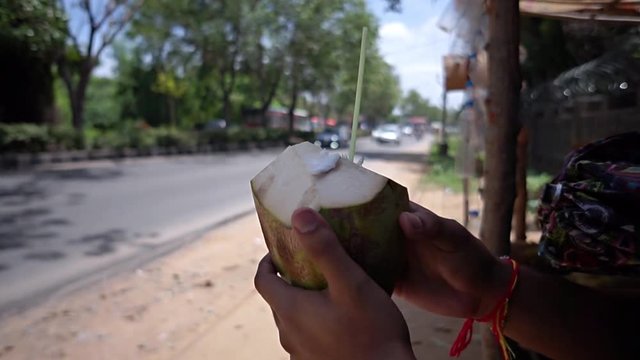 A man holding and about to drink coconut water nutty elixir beside a busy road no face