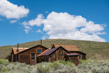 Abandoned, weathered, wood-sided buildings and homes under a beautiful blue sky with puffy white clouds in the ghost town of Bodie, California