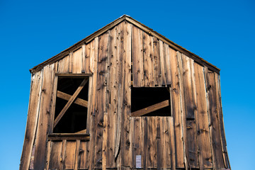 Fototapeta premium Abandoned rustic wood shack under pertfect bright blue sky in the ghost town of Bodie, California