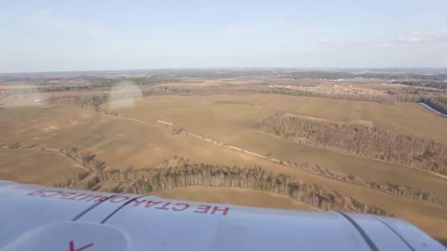 Helicopter flight in clear, warm, sunny weather, over forests, fields and populated areas. View from the airplane window.