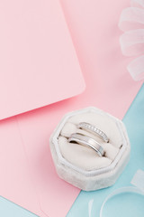 Two silver wedding rings with diamonds on pink background