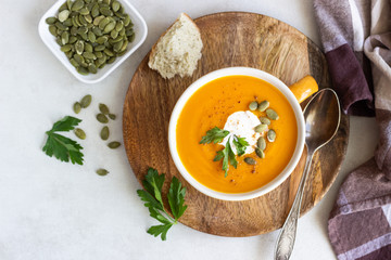 Roasted pumpkin soup with cream, parsley and pumpkin seeds on light background. 