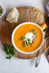 Roasted pumpkin soup with cream, parsley and pumpkin seeds on light background. 