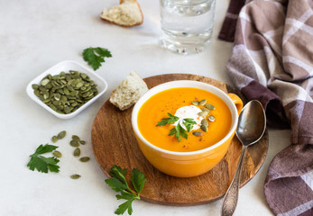 Roasted pumpkin soup with cream, parsley and pumpkin seeds on light background. 