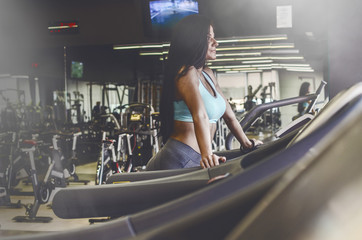 Fototapeta na wymiar Girl walking in gym on treadmill