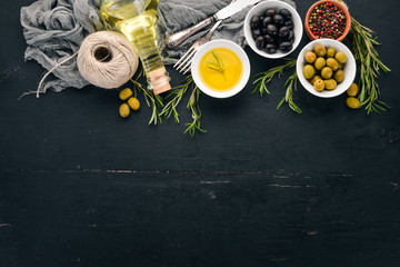 A set of olives and olive oil and rosemary. Green olives and black olives. On a black wooden background. Free space for text.