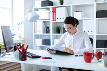 A young girl sits in the office, holds a pen in her hand and looks through documents.