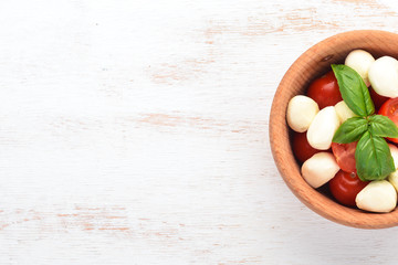 Mozzarella cheese, cherry tomatoes in a wooden plate. Salad caprese On a white table. Free space for text.