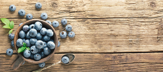 Freshly picked blueberries on rustic aged wooden table surface. Flat lay. Ripe blueberry with leaves in ceramic jar and also scattered around  with copy space.