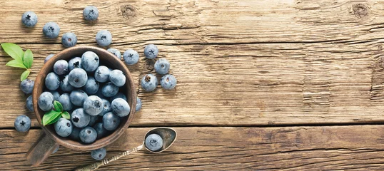 Fotobehang Freshly picked blueberries on rustic aged wooden table surface. Flat lay. Ripe blueberry with leaves in ceramic jar and also scattered around  with copy space. © stone36