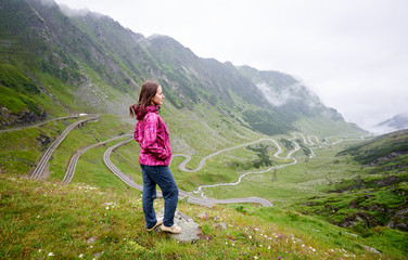Shot of a female traveller smiling looking away standing on the hill in front of the Transfagarasan road copyspace Romanie travelling destinations tourism active lifestyle location.