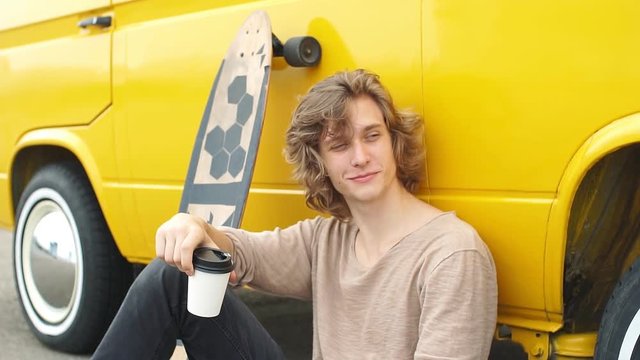 stylish young blond curly hair man sitting on longboard and using smartphone and smile