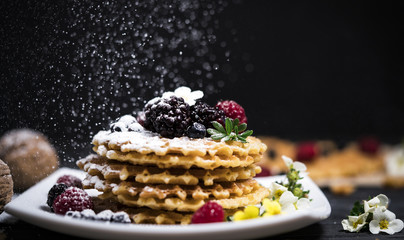 fresh viennese waffles with berries sprinkled with powdered sugar on blackboard on blank background
