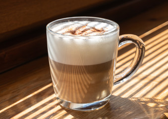 Cup of latte on the wooden background in a harsh light