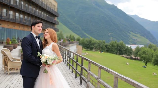 Beautiful bride and groom stand on the open terrace near the hotel in the background of the mountains. Georgia Kazbegi