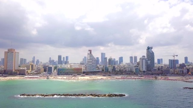 Aerial footage of Tel Aviv's skyline along the coastline with people at the beach on a summer's day