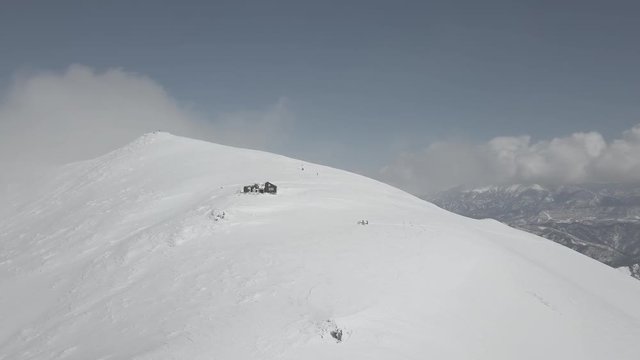 Drone shoot of a shelter in the top of a japan mountain during winter, a group of skier is under