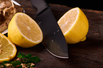 Cutted lemon with spices and herbs on a wooden background with black knife